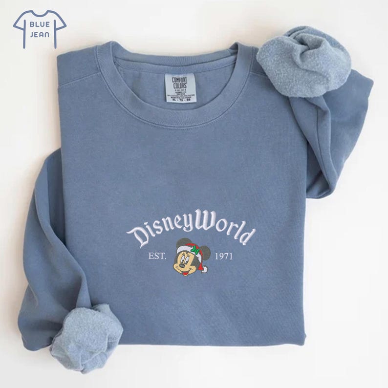 May include: A blue crew neck sweatshirt featuring the text "DisneyWorld" in white script, and an image of Mickey Mouse in a Santa hat. The sweatshirt also has the text "EST. 1971".