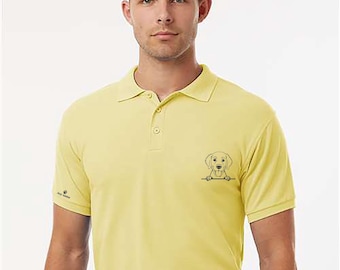 May include: A light yellow polo shirt with a black and white Labrador Retriever graphic on the chest. The shirt has a classic collar, short sleeves, and a three-button placket. The model is wearing a black belt and navy blue pants.
