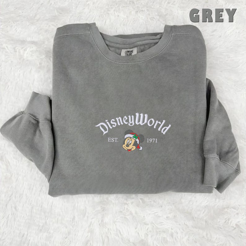 May include: A grey sweatshirt featuring white embroidered text reading "DisneyWorld", "EST. 1971", and a Mickey Mouse graphic in a Santa hat. The word "GREY" is printed in the upper right corner.