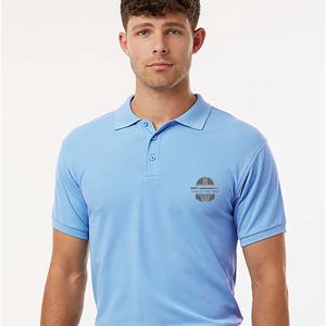 K&ouml;nnte beinhalten: Hellblaues Poloshirt mit kurzen &Auml;rmeln und Kragen. Das Shirt hat eine Knopfleiste mit drei Kn&ouml;pfen und ein kleines Logo auf der linken Brust. Das Logo enth&auml;lt den Text "THIS IS THE WAY".