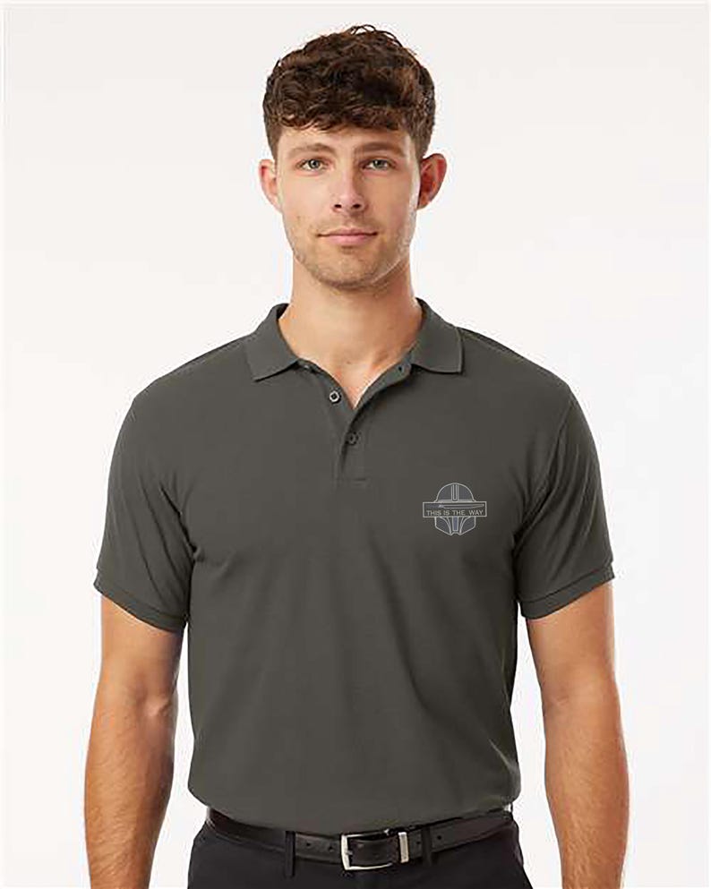 K&ouml;nnte beinhalten: Dunkelgraues Poloshirt mit kurzen &Auml;rmeln und Kragen. Das Shirt hat eine kleine, hellgraue Grafik auf der Brust mit dem Text "THIS IS THE WAY". Das Shirt hat ein klassisches Design mit Kn&ouml;pfen und ist aus weichem Material gefertigt.