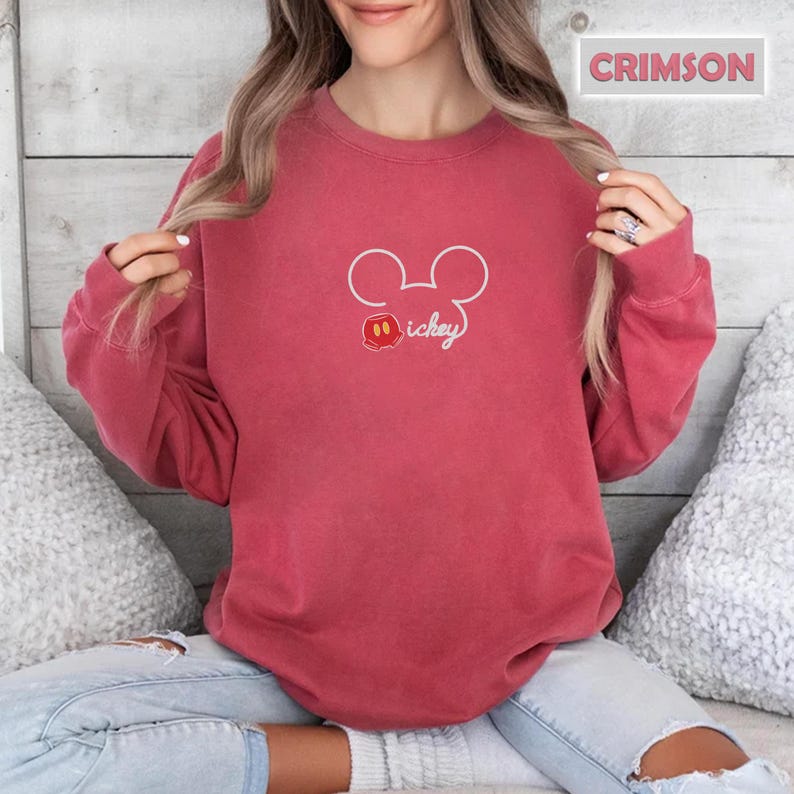 Peut inclure: Sweat-shirt de couleur cramoisie avec un contour blanc des oreilles de Mickey Mouse et le mot "Mickey" en cursive. Le motif comprend une petite t&ecirc;te de Mickey Mouse rouge, noire et blanche. Le sweat-shirt est de couleur unie.
