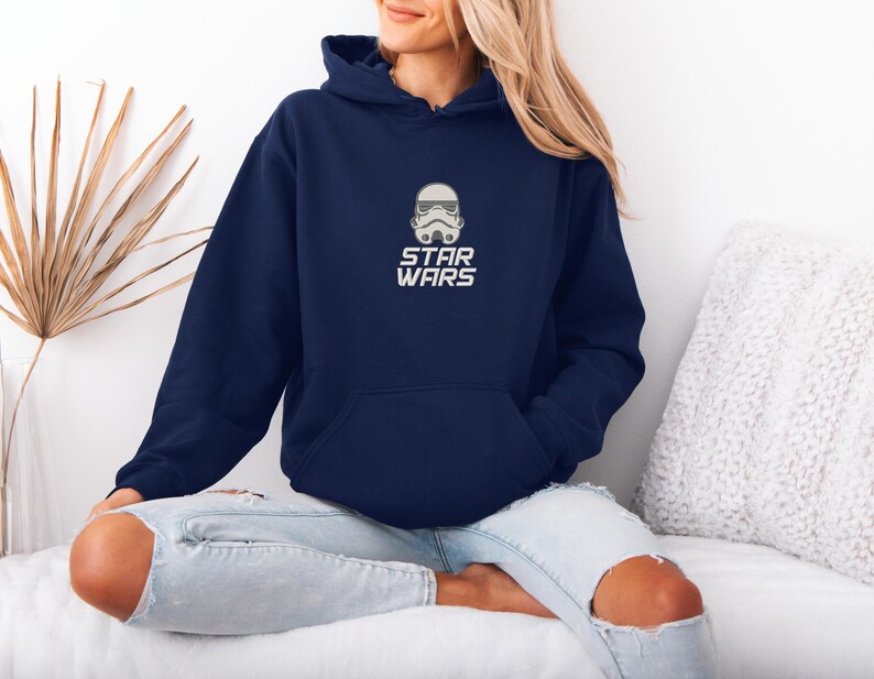 May include: Navy blue hooded sweatshirt featuring a white Stormtrooper helmet graphic and the words "STAR WARS" in white. The sweatshirt has a front pocket and a drawstring hood. The design is centered on the chest.