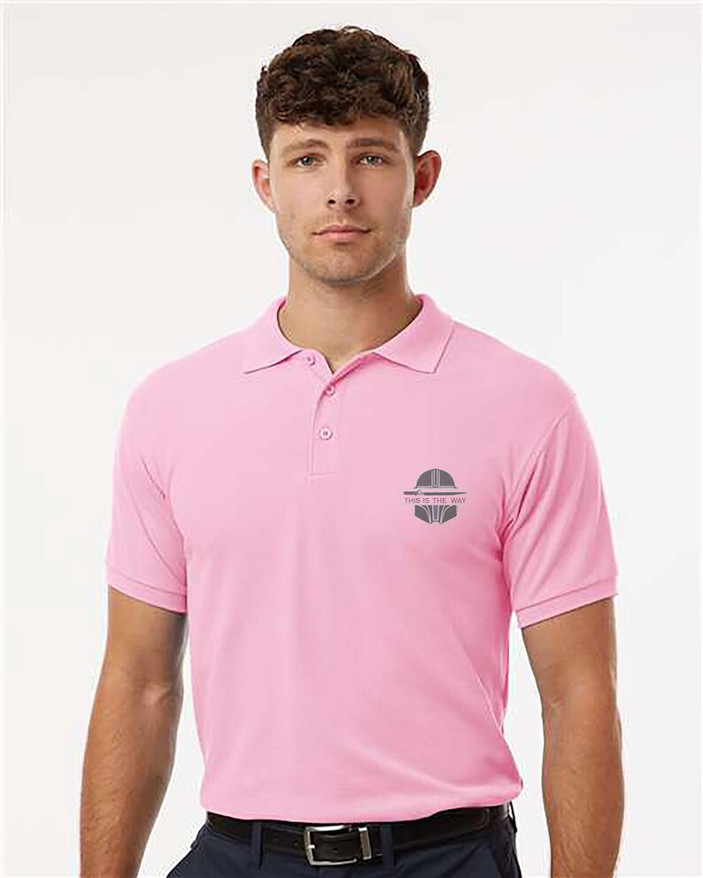 K&ouml;nnte beinhalten: Hellrosa Poloshirt mit kurzen &Auml;rmeln und Kragen. Das Shirt hat eine kleine graue Grafik und den Text "THIS IS THE WAY" auf der linken Brust. Das Shirt ist aus einem weichen Material.
