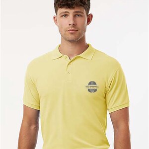 K&ouml;nnte beinhalten: Hellgelbes Poloshirt mit kurzen &Auml;rmeln und Kragen. Auf der Brust befindet sich eine kleine Grafik mit dem Text "THIS IS THE WAY". Das Shirt wird mit einer dunkelblauen Hose und einem schwarzen G&uuml;rtel getragen.