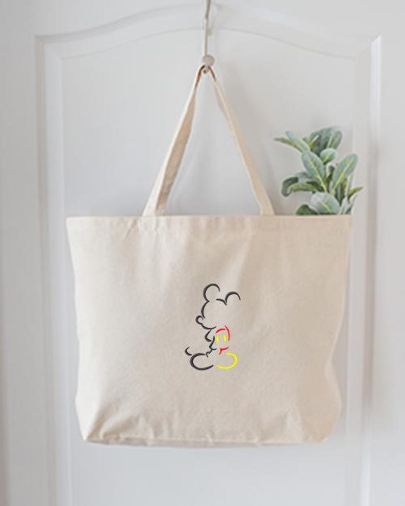 May include: A beige canvas tote bag with a black, red, and yellow outline of a cartoon mouse. The bag is hanging on a white door. A small green plant is visible inside the bag.