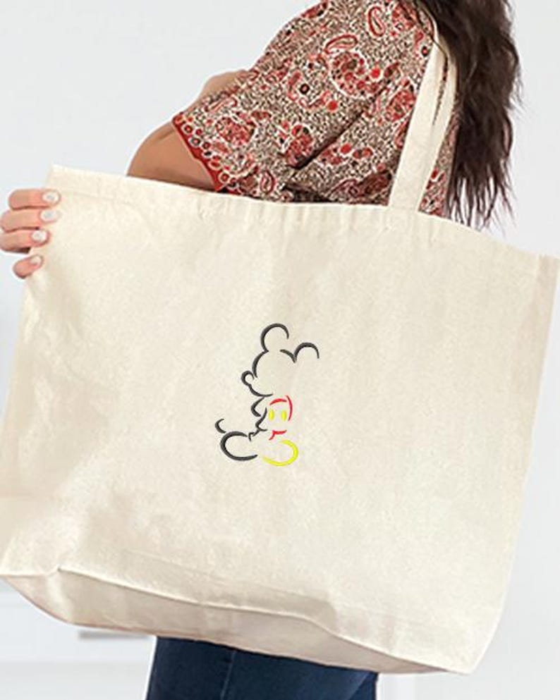 May include: Cream-colored tote bag with a black, red, and yellow outline of Mickey Mouse. The bag has long straps and is made of a sturdy fabric, suitable for carrying groceries or other items. The design is simple and classic.