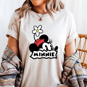 May include: White t-shirt with a cartoon image of Minnie Mouse wearing a red bow and a flower on her head. The text "MINNIE" is printed below the image.