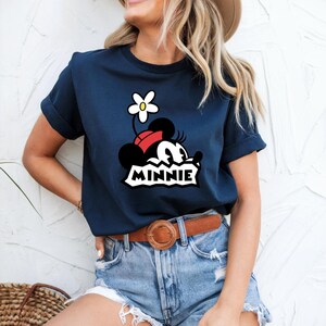 May include: A navy blue t-shirt with a cartoon image of Minnie Mouse wearing a red bow and a white flower. The text "MINNIE" is printed below the image.