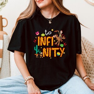 May include: Black t-shirt with a graphic of Woody from Toy Story riding a horse with the text "to infinity and beyond" in orange and yellow rope.
