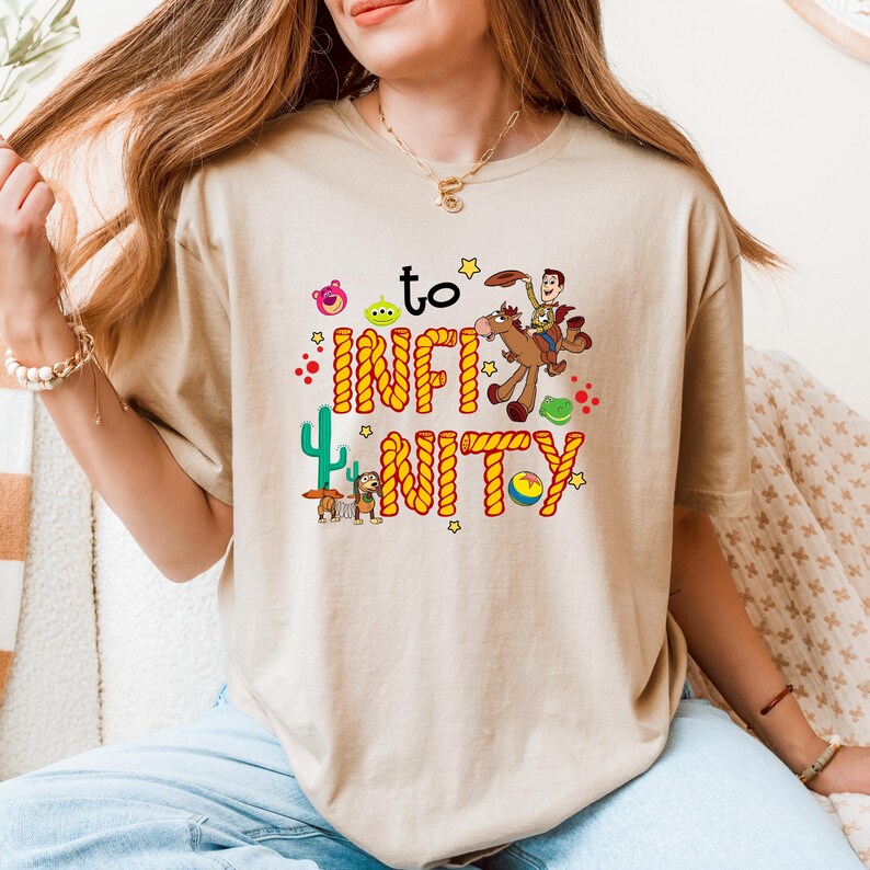 May include: A beige t-shirt with a graphic of Woody from Toy Story riding a horse with the text "to infinity and beyond" in a rope design.