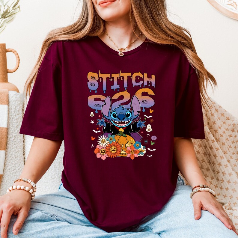 Puede incluir: Camiseta burdeos con un dise&ntilde;o de Stitch de Lilo & Stitch, disfrazado de vampiro, y el texto "Stitch 626". El dise&ntilde;o incluye una calabaza, flores y elementos tem&aacute;ticos de Halloween.