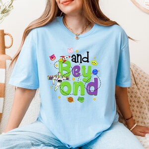 May include: Light blue t-shirt with a graphic of Buzz Lightyear, a rocket, and the text "and Beyond" in green, purple, and black.