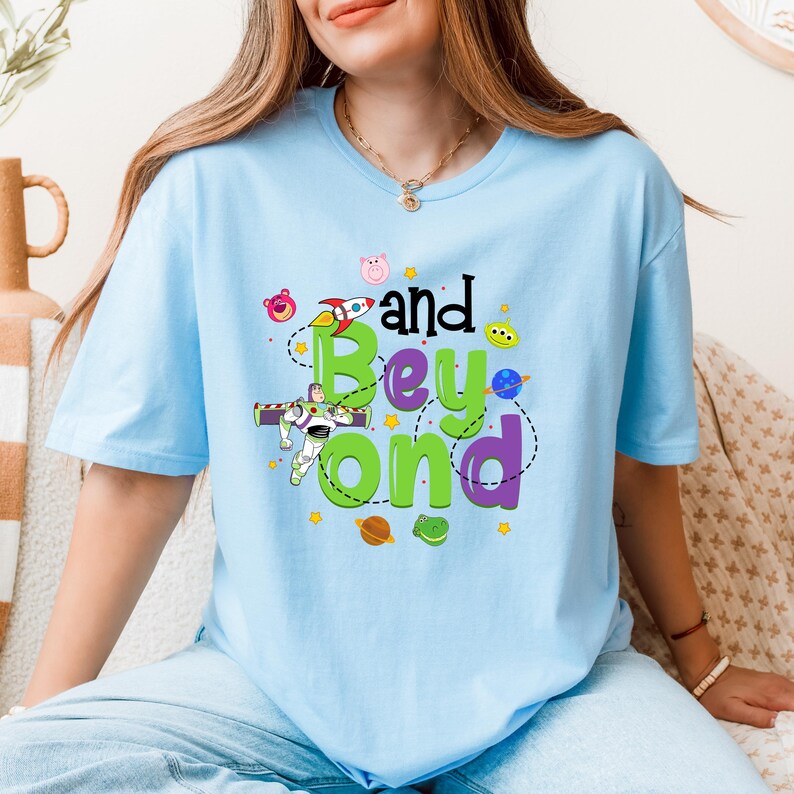 May include: Light blue t-shirt with a graphic of Buzz Lightyear, a rocket, and the text "and Beyond" in green, purple, and black.