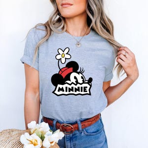 May include: A gray t-shirt with a cartoon image of Minnie Mouse wearing a red bow and a white flower on her head. The text "MINNIE" is printed below the image.