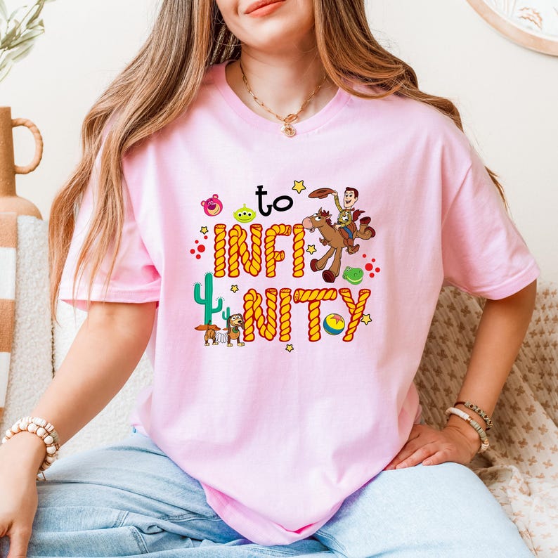 May include: Pink t-shirt with a graphic of Woody from Toy Story riding a horse with the text "to infinity and beyond" in a rope design.