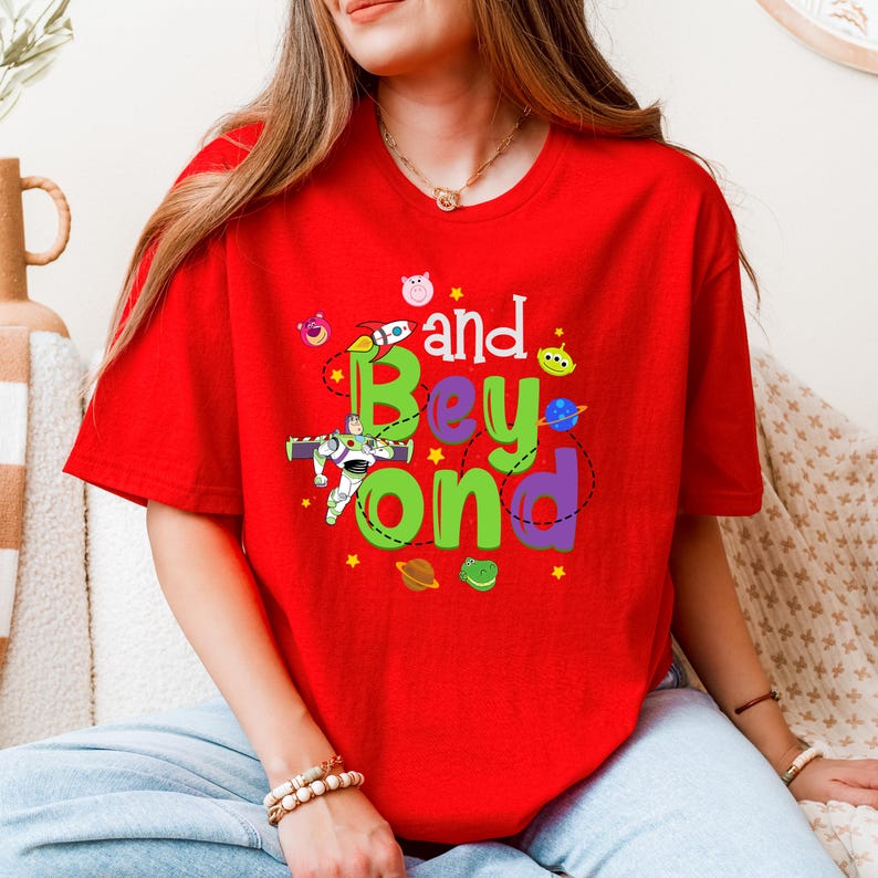 May include: Red t-shirt with a green and purple graphic that says "and Beyond" with cartoon characters from the Toy Story movie franchise.