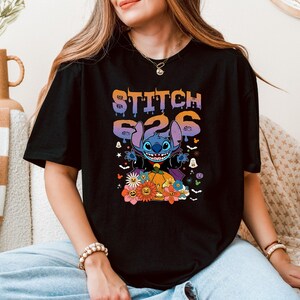 Puede incluir: Camiseta negra con un gr&aacute;fico colorido de Stitch de Lilo & Stitch. El dise&ntilde;o incluye el texto "STITCH 626" encima de Stitch, rodeado de elementos tem&aacute;ticos de Halloween como calabazas, flores y fantasmas.