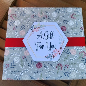 May include: A gray gift box with a floral pattern and a red ribbon. The box has a hexagonal tag with the text "A Gift For You" and floral illustrations.