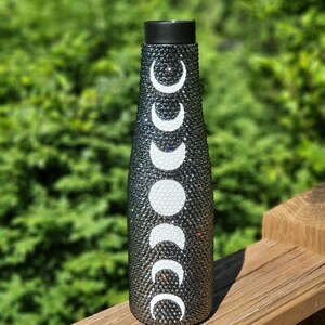 May include: A black water bottle with a silver glitter finish and a white moon phase design.