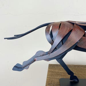 May include: A metal sculpture of a horse in motion. The sculpture is made of interwoven metal strips, with a color scheme of black and reddish-brown. The horse's tail is made of thin, black metal rods. The sculpture is mounted on a black base.