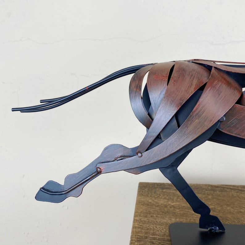 May include: A metal sculpture of a horse in motion. The sculpture is made of interwoven metal strips, with a color scheme of black and reddish-brown. The horse's tail is made of thin, black metal rods. The sculpture is mounted on a black base.