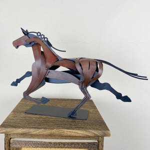 May include: A metal sculpture of a running horse. The sculpture is made of brown and black metal pieces, with a detailed mane and tail. The horse is mounted on a black rectangular base.