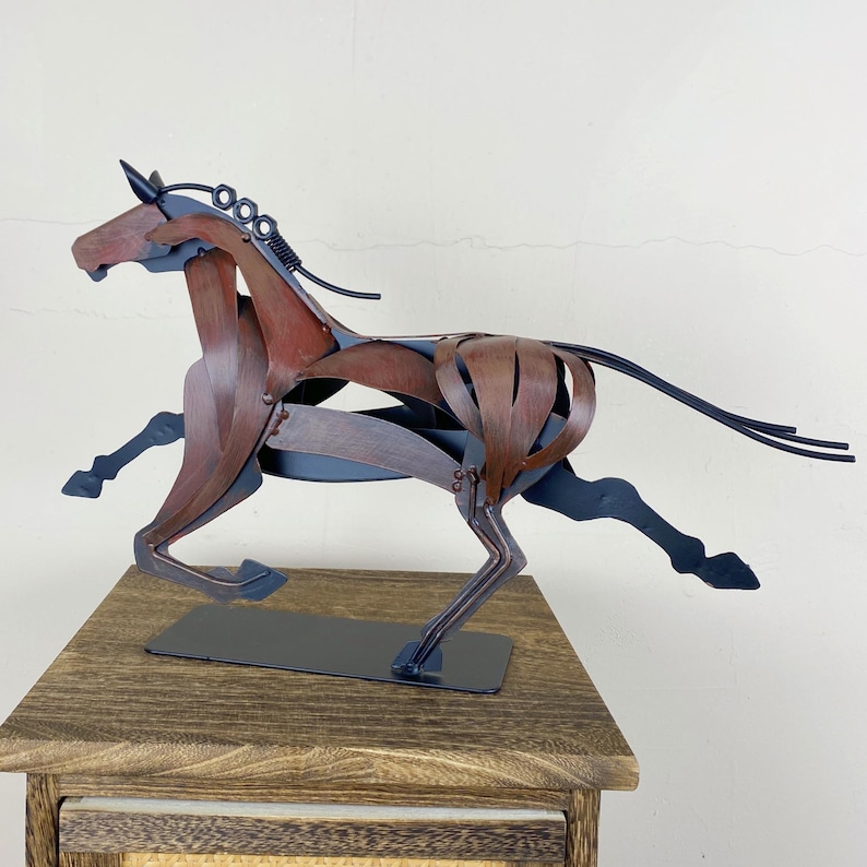 May include: A metal sculpture of a running horse. The sculpture is made of brown and black metal pieces, with a detailed mane and tail. The horse is mounted on a black rectangular base.