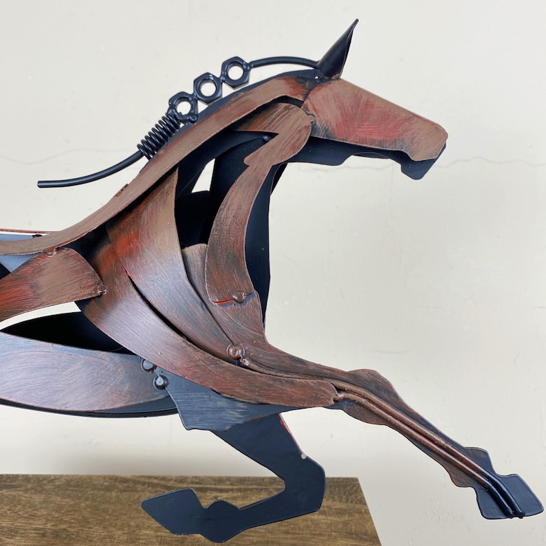 May include: A metal sculpture of a horse in a running pose. The sculpture is made of various metal pieces, with a color scheme of brown, black, and red. The horse's mane is made of a black spring and metal pieces.