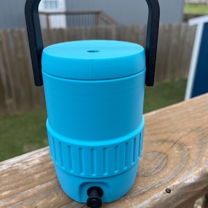 May include: A bright cyan beverage cooler featuring a cylindrical body with a textured middle band, a solid lid with a small central opening, and a black plastic handle attached to the sides. A small black spigot is located at the base.