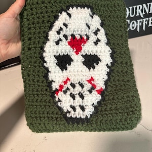 May include: Green crocheted pot holder with a white, black, and red crocheted hockey mask design.