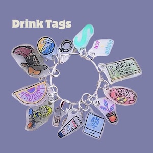 Puede incluir: Un brazalete de plata con varios dijes, incluyendo un sombrero de bruja, una luna creciente, una planta, un logotipo de caballos voladores y un logotipo de casa de panqueques. Los dijes están unidos a una cadena de plata.