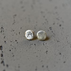 May include: Two silver earrings with the letters A and M engraved on them.