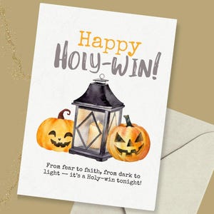 Puede incluir: Una tarjeta de felicitación de Halloween con las palabras "Happy Holy-Win!" en naranja y gris. La tarjeta presenta una linterna negra con velas encendidas y dos calabazas talladas. También se incluye el texto "From fear to faith, from dark to light - it's a Holy-win tonight!"