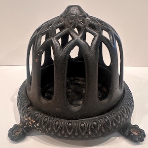 May include: A black, cast iron decorative cage with an ornate design. The cage has a domed top and is supported by a base with decorative detailing and claw feet. The cage is likely for decorative purposes.
