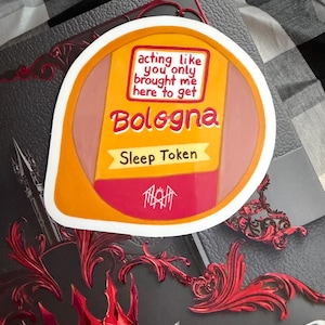 Peut inclure: Un autocollant découpé en forme de tranche de mortadelle avec une étiquette jaune et rouge. Le texte indique : acting like you only brought me here to get Bologna, Sleep Token, et un symbole en ligne blanche en bas sur fond rouge.