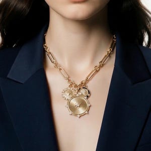 May include: A gold-toned necklace with multiple charms. The necklace features a large, round pendant with a starburst design and small, clear stones. Additional charms include a sunburst and a circular design with black and white accents.
