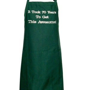 Puede incluir: Un delantal verde oscuro con un bolsillo blanco y el texto "It Took 70 Years To Get This Awesome!" bordado en la parte delantera.