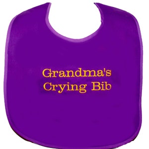 May include: Purple baby bib with yellow embroidery that reads "Grandma's Crying Bib".