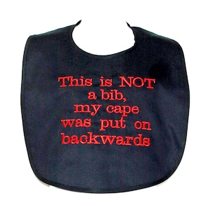 May include: Black bib with red embroidered text that reads "This is NOT a bib, my cape was put on backwards".