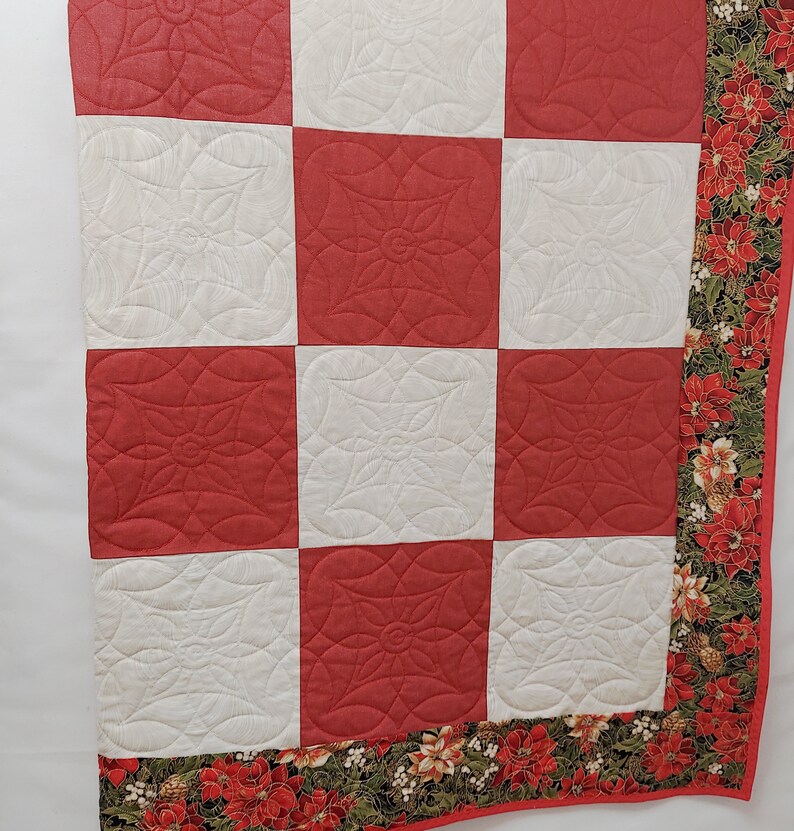 May include: A red and white quilt with a poinsettia print border. The quilt is made of squares with a quilted design of a flower.