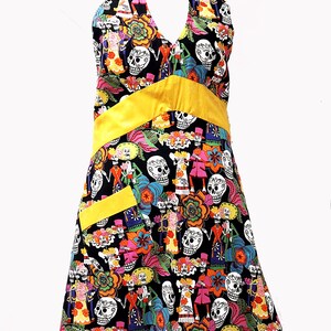 May include: A black halter dress with a yellow sash and a colorful print of skeletons and flowers. The dress has a small yellow pocket on the front.