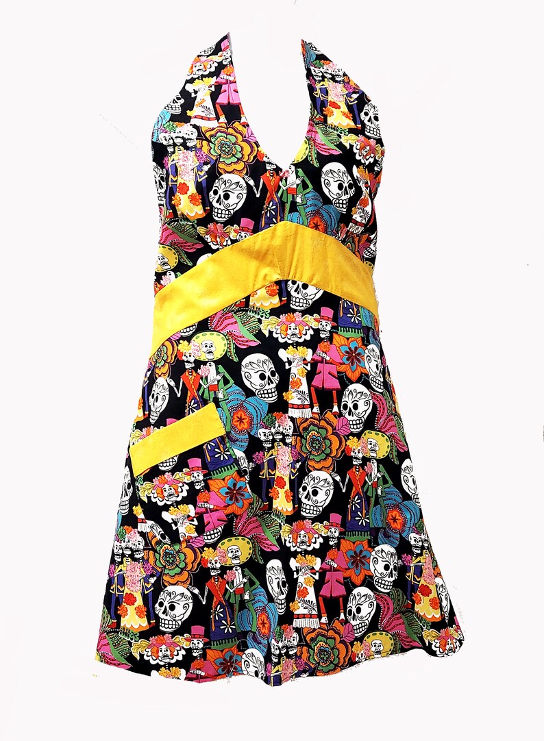 May include: A black halter dress with a yellow sash and a colorful print of skeletons and flowers. The dress has a small yellow pocket on the front.
