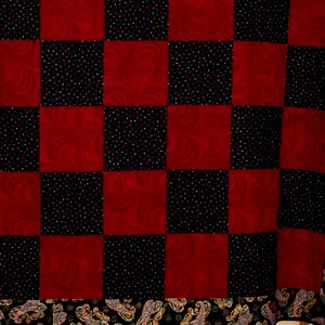 May include: A red and black checkered quilt with a paisley border. The quilt is made of fabric with a swirl pattern and a black fabric with small colorful dots.