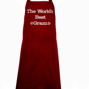 May include: Red kitchen apron with white text that reads "The World's Best Gram" with a heart symbol before and after the word "Gram".