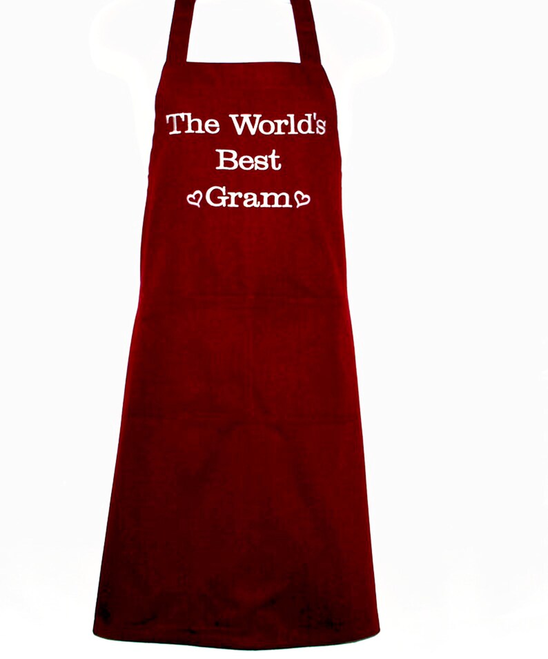 May include: Red kitchen apron with white text that reads "The World's Best Gram" with a heart symbol before and after the word "Gram".