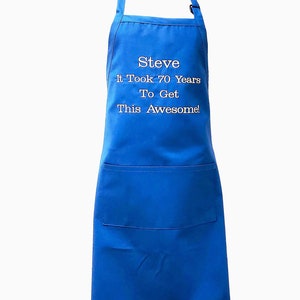 Puede incluir: Delantal de algod&oacute;n azul con un bolsillo grande. El delantal tiene bordado blanco que dice "Steve It Took 70 Years To Get This Awesome!"