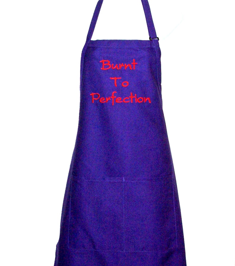 Pode incluir: Avental roxo com o texto "Burnt To Perfection" bordado em vermelho. Possui um bolso e uma al&ccedil;a de pesco&ccedil;o ajust&aacute;vel. Acess&oacute;rio de cozinha para cozinhar e assar.