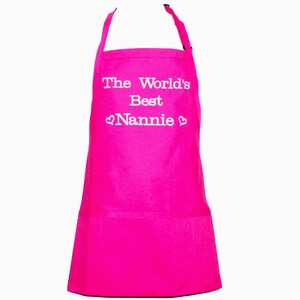 May include: A pink apron with a white pocket and the text "The World's Best Nannie" with a heart on each side of the word "Nannie".