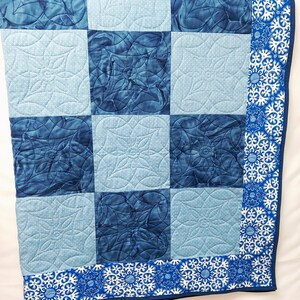 May include: A blue and white quilt with a floral pattern. The quilt is made of squares with different shades of blue and white. The border of the quilt is a white fabric with a blue floral pattern.